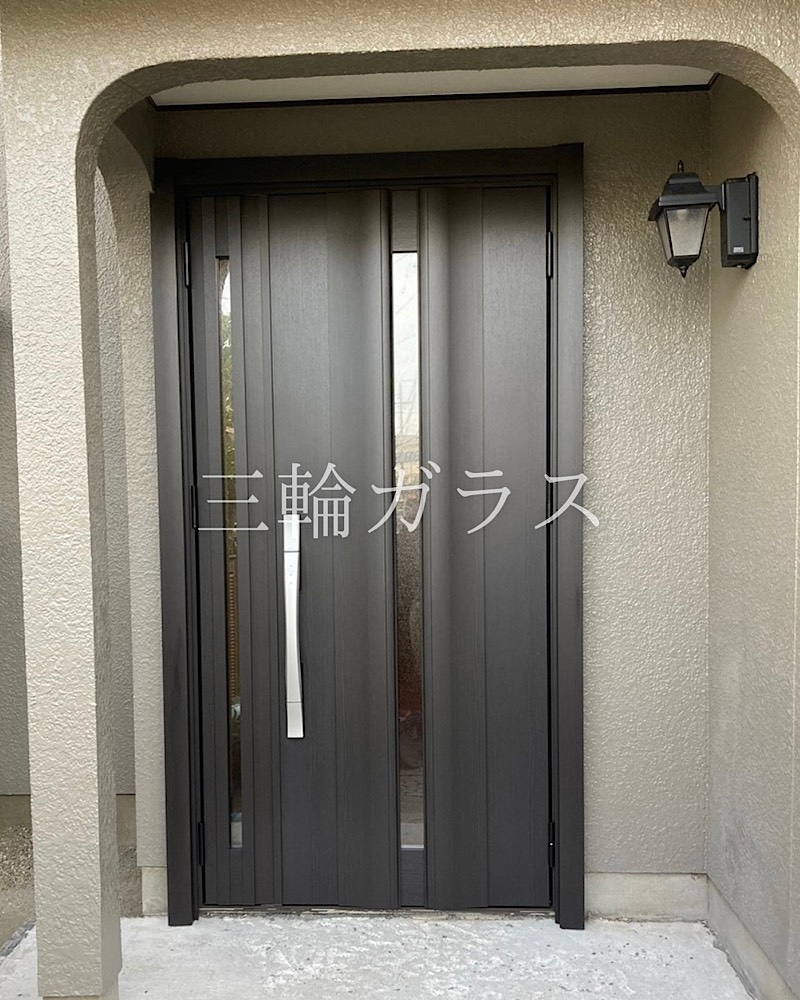 「街の玄関ドアやさん豊明店」のブログ記事用として、指定の画像（chita-lixil-rechent-reform-g12-before-after-miwaglass-03.jpg.jpg）に関するテキストを作成しました。 代替テキスト (Alt Text) LIXILの断熱玄関ドア「リシェント3」G12型（トリノパイン色）が設置された施工途中の様子。ドア本体と子扉に縦長の採光ガラスがあり、シルバーのS型ハンドルが取り付けられている。足元のポーチ部分はタイルを貼る前のコンクリート下地の状態。