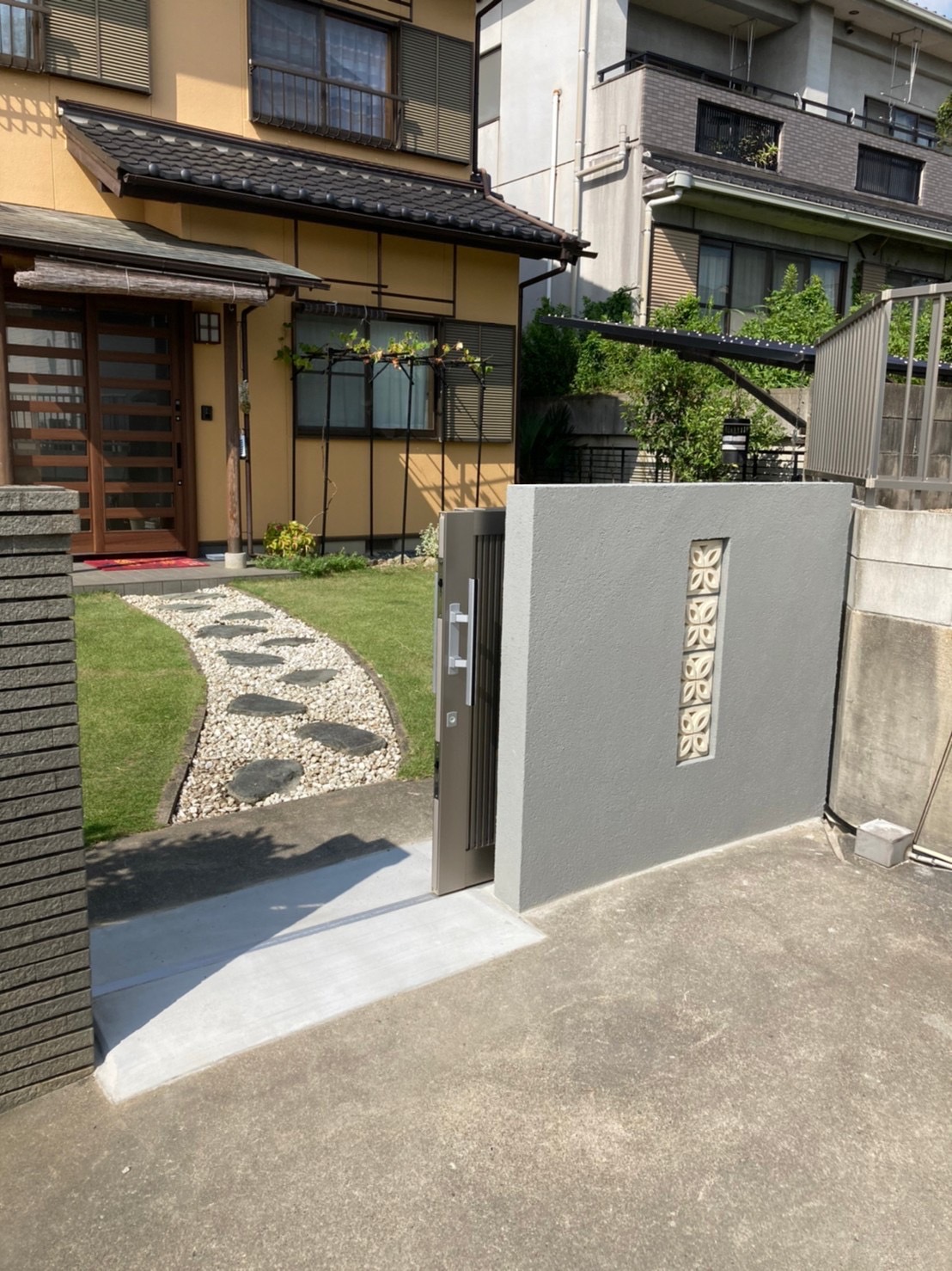 大府市の木造建築。スライド門扉が開き、奥にリフォーム済みのLIXILリシェント玄関引戸、芝生と飛び石（平板）のアプローチが見える全体像。